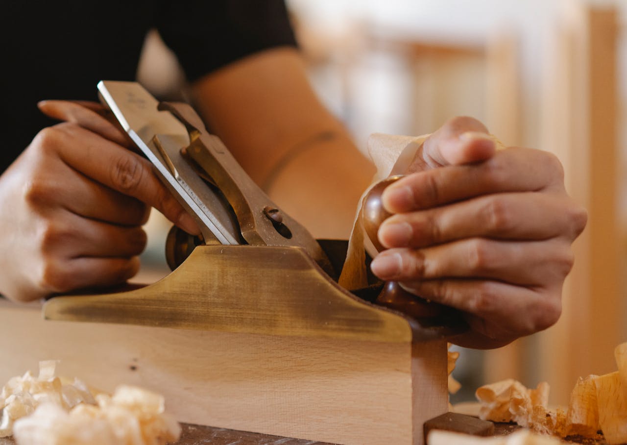 Close-up of craftsman using a hand plane for precise woodwork in an indoor workshop.